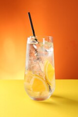 Refreshing soda water with orange slices and ice cubes in glass on yellow table against orange background