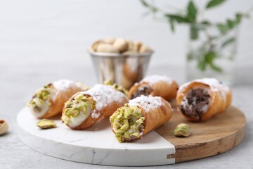 Delicious cannoli with ricotta cheese, pistachios, chocolate and powdered sugar on light grey table indoors, closeup