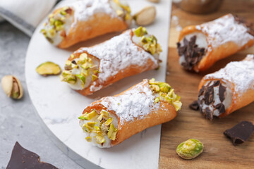 Delicious cannoli with ricotta cheese, pistachios, chocolate and powdered sugar on grey table, closeup