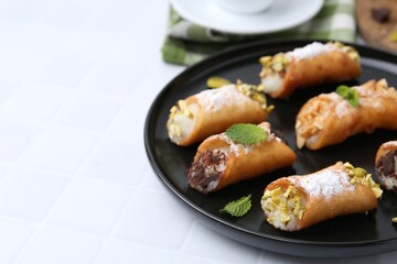 Delicious cannoli with cheese, nuts, powdered sugar, chocolate and mint on white tiled table, closeup. Space for text