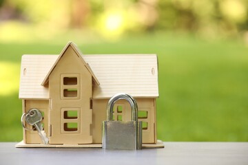 Home security. House model, key and padlock on light table outdoors, closeup. Space for text