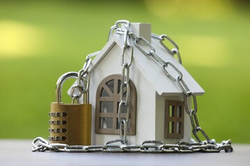 Home security. House model, chain and padlock on light grey table outdoors, closeup