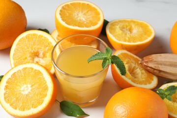 Freshly squeezed orange juice, fruits and juicer on white table, closeup