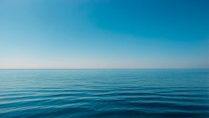 Obraz premium The horizon line divides the deep blue ocean from a gradient sky. A serene seascape with calm rippling waters under a clear sky. Peaceful atmospheric landscape.