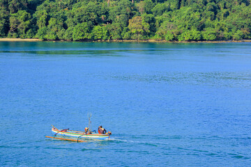 Traditional Fishing Boat Sailing on Calm Blue Ocean with Lush Green Shoreline