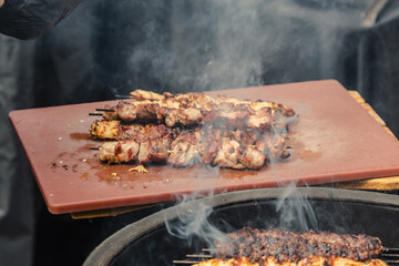 Juicy skewered meat grilled on a board and ready to eat during barbecue with smoke rising