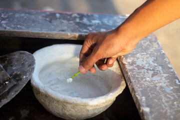 A hand stirs a white substance in a bowl with a small green tool