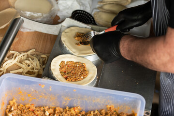 A person wearing black gloves is preparing empanadas, baked or fried turnover consisting of pastry and filling, common in Spain, other Southern European, and Latin American countries