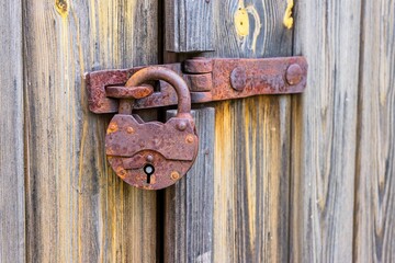 Close-up of an old rusty padlock on a wooden door with brick wall in the background, symbol of security, restriction and time.