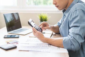 Fototapeta premium Saving money wealth concept, asian young business man, male using calculator for calculate saving cost, cash finance planning to spend enough money on his income for save money, payment tax, investing