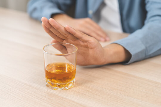 Alcoholism, depressed asian young man refuse, push out alcoholic beverage glass, drink whiskey, sitting alone at night. Treatment of alcohol addiction, having suffer abuse problem alcoholism concept.