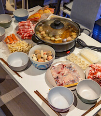 Hot pot meal spread with assorted raw ingredients including sliced meat, mushrooms, dumplings, and seafood balls, ready for cooking at home