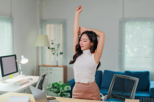 Young Asian businesswoman is relaxing and stretching her arms at workplace after work is finished