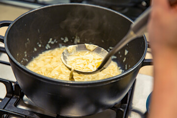 Hot black pot on stove with sweet egg drop soup being ladled out, showing glutinous rice balls and tofu skin in a warm dessert preparation