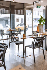 Spacious cafe interior with wooden tables and modern black chairs, large windows letting in daylight, street view in background
