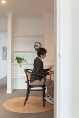 Person sitting at a small desk reading in a minimalist modern home interior with white walls, built-in shelves, and natural decor elements