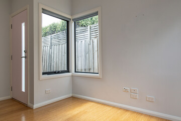 Compact living space featuring bamboo flooring, pastel front door, and dual windows with outdoor fence views, suited for small modern homes