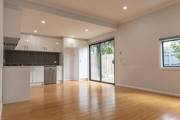 Open-plan kitchen and living area in a modern home with white cabinets, dark backsplash tiles, bamboo floors, and sliding door access to outdoor space