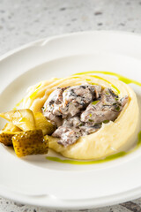 Gourmet dish with creamy purée, mushroom cream sauce, artichoke hearts, and herb oil drizzle on elegant white plate, styled on stone surface