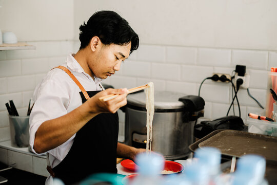 Southeast Asian chef cooking noodles with chopsticks in the kitchen