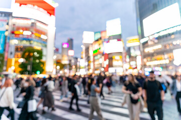 Blurred image of crowd of people crossing Shibuya Scramble Crossing with illuminated billboards in Tokyo at night