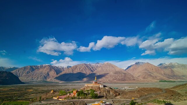 A majestic statue of Maitreya Buddha seated in a meditative pose against the backdrop of the rugged Himalayas and a clear blue sky. This vibrant monument, located in Diskit Monastery, Nubra Valley,