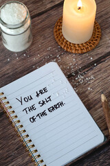 You are the salt of the earth, handwritten text with candle light on wooden background. Top view. Christian biblical concept.