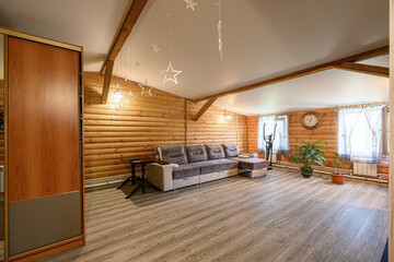 Cozy living room with log walls, a sectional sofa, wooden floor, and decorative star lights. Bright and inviting space