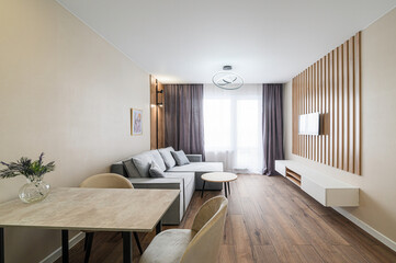 Cozy living room with gray sofa, dining table, wood accents, and TV. Modern lighting and neutral color scheme