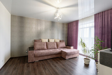 Cozy living room featuring a brown sectional sofa, grey accent wall, and purple curtains, with plants adding a touch of nature
