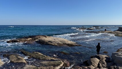 People fishing on rocky seaside under blue sky