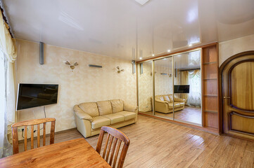 Cozy living room with a beige leather sofa, wooden table and chairs, mirrored closet and glossy ceiling
