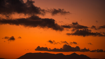 Scenic view of mountain silhouette with dramatic orange sunset sky and dark clouds in the evening light nature background  
