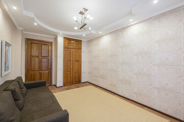 living room with a brown sofa, beige carpet, patterned wallpaper, wooden doors, and a decorative ceiling with lighting