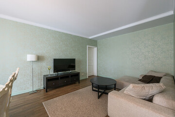 Cozy living room with patterned walls, TV, sofa, rug, and round table. Lamp provides soft lighting