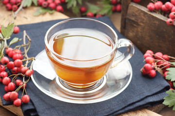 Haw thorn autumn berry tea in a glass cup on rustic background, red herbal drink against heart disease, insomnia, neurosis and hypertension, closeup, copy space, naturopathy concept
