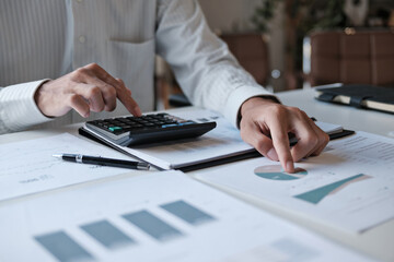 Administrative staff reviewing company budget report with calculator, document stack and focus at...
