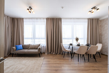 cozy living/dining area with a sofa, round table with four chairs, large windows, and neutral color palette