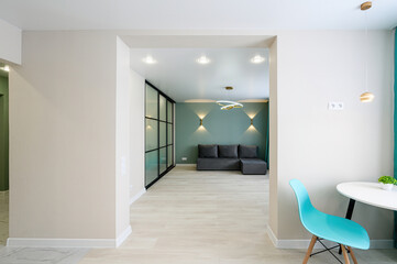 open doorway reveals a stylish living area with a gray sofa, green walls, modern lighting, and a sliding glass door. A blue chair sits near a table in the foreground