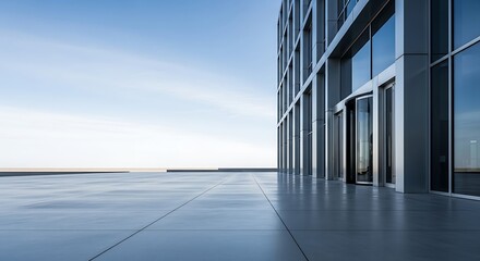 Exterior of a modern office building with a glass facade and an empty plaza under a clear blue sky.