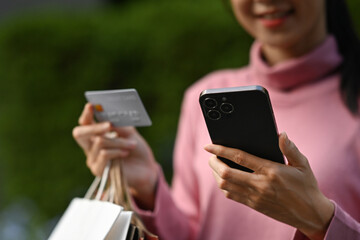 Close-up of a woman holding a credit card and smartphone, making an online purchase outdoors
