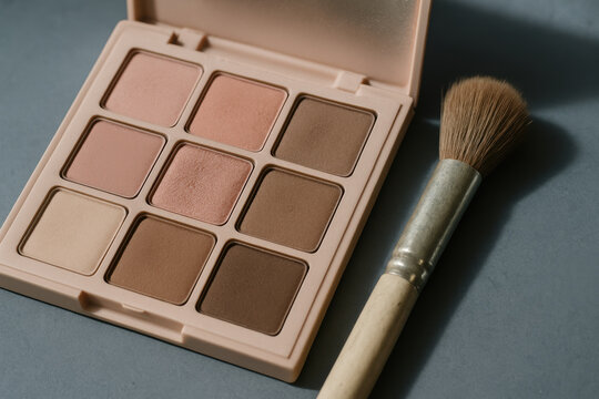 Neutral matte eyeshadow palette with brush on gray surface, ideal for natural makeup looks and modern beauty trends