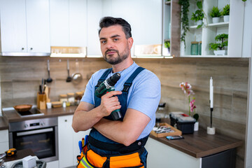Skilled handyman posing confidently in modern kitchen with power drill ready for tasks