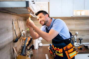 Man repairs kitchen light fixture while smiling in modern apartment