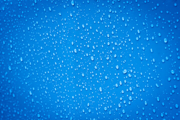 A vibrant blue surface covered in a mesmerizing array of water droplets of varying sizes, creating a dynamic texture and abstract pattern