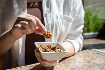 Female hand holding walnut from small dish with walnuts. Concept of memory support, cognitive health and natural superfood.
