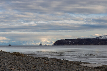 Gertner Bay, Sea of ​​Okhotsk, Magadan Region, Far East of Russia. Beautiful evening seascape. View from the stony shore to the sea bay. Rocky islands and mountains in the distance. Cloudy weather.