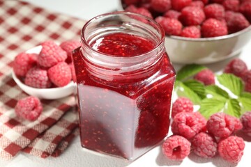 Delicious raspberry jam in glass jar, fresh berries and mint on white table, closeup