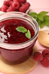 Sweet raspberry jam in glass jar, berries and mint on pink wooden table, closeup