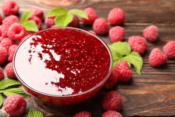 Delicious raspberry jam in glass bowl, fresh berries and mint on wooden table, closeup